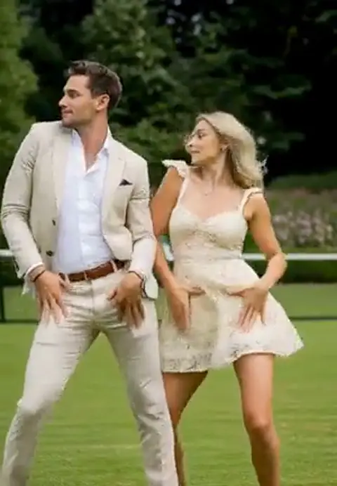 A couple in cream and white summer outfits dance a playful routine in sync on a green lawn, trees and hedges behind them, bright daylight, full body vertical video.